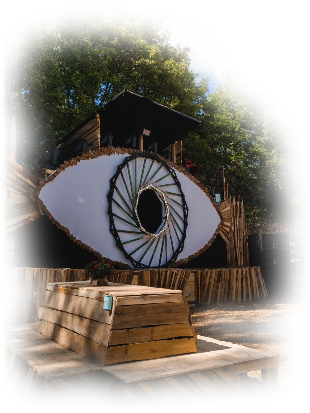 Festivalbühne aus Holz in Form eines großen Auges, davor Sitzbänke aus Holz, bei Tageslicht